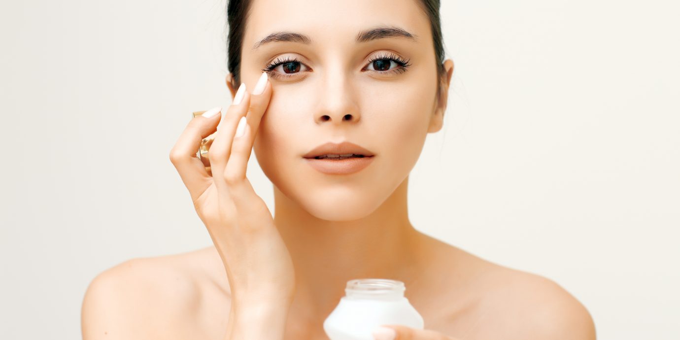 Natural beauty portrait of young woman applying cream on her face, Eye creams with SPF