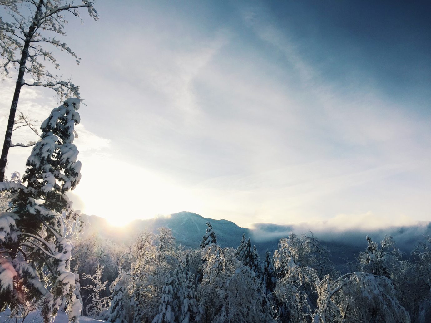 Looking eastward toward the mountains near Smuggler's Notch in Vermont in wintertime. The sun is rising and partially visible as it crests the hills. The trees are covered in hoarfrost.