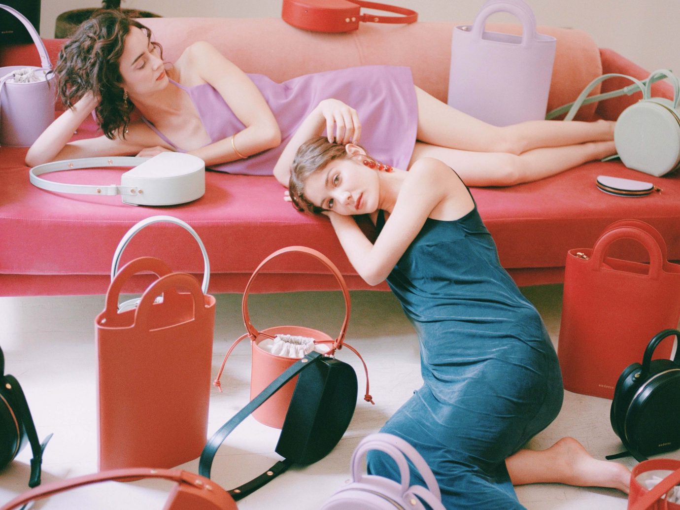 Two women modeling purses on a red couch
