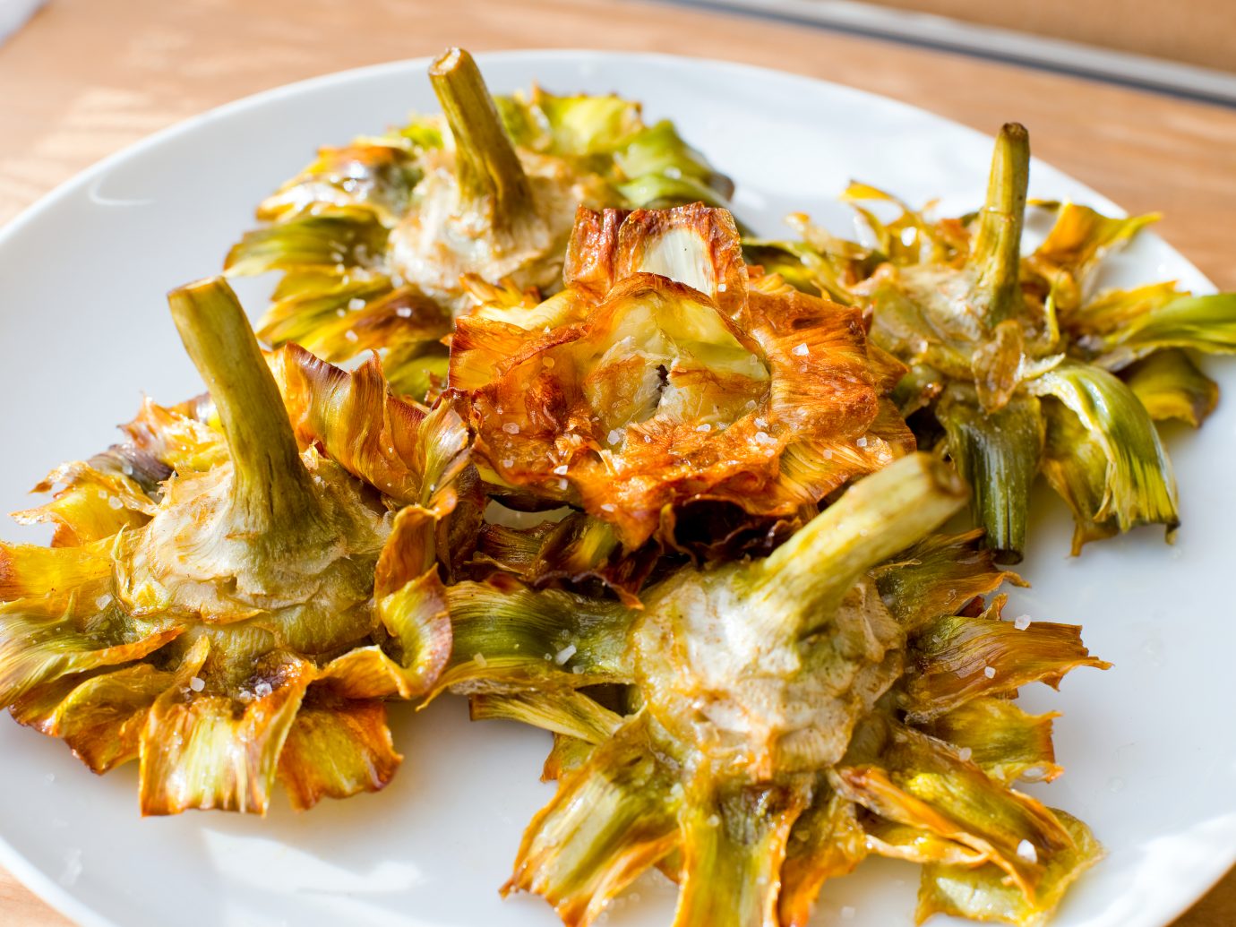 Roman fried artichokes (jewish style) with flakes of sea salt on a wooden table.