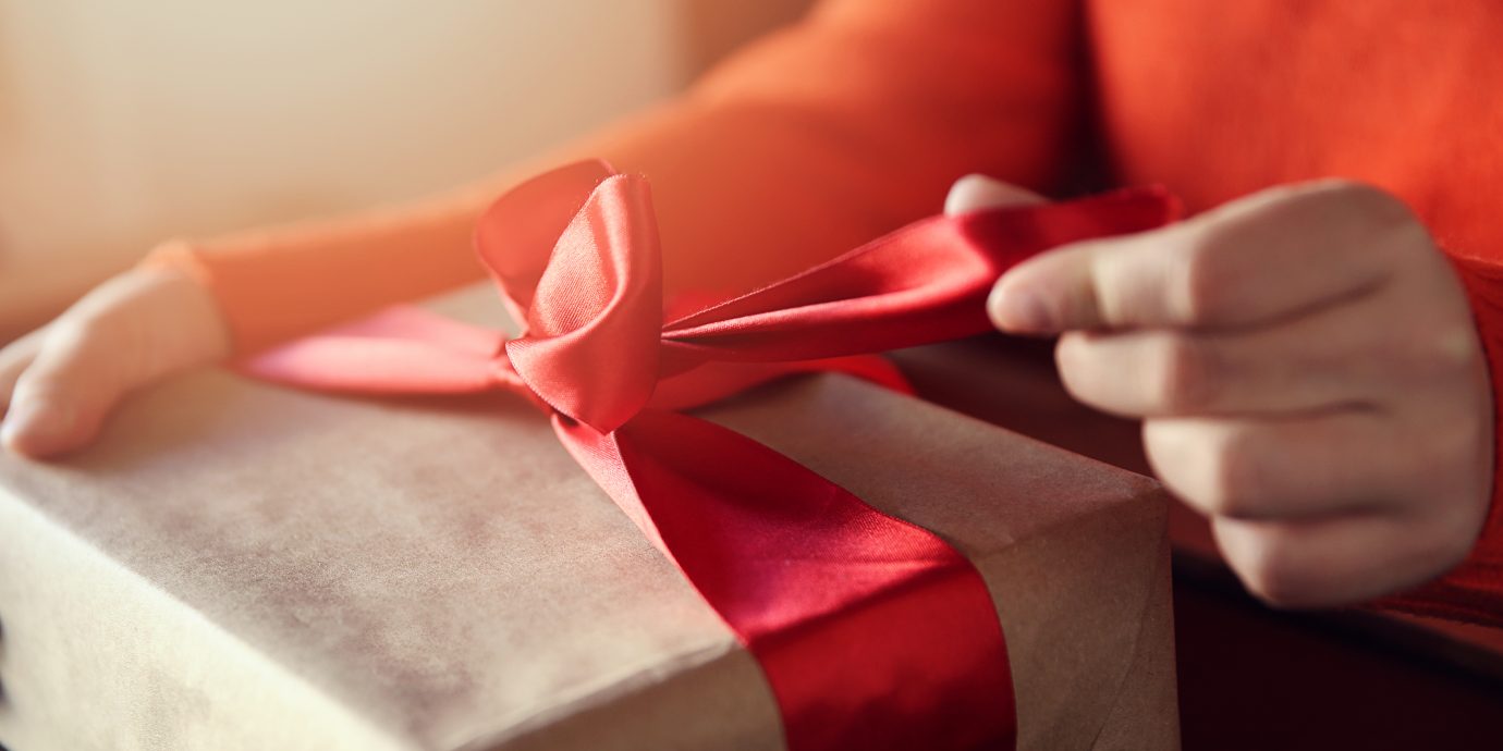 Hand pulls red ribbon on a gift wrapped in brown paper