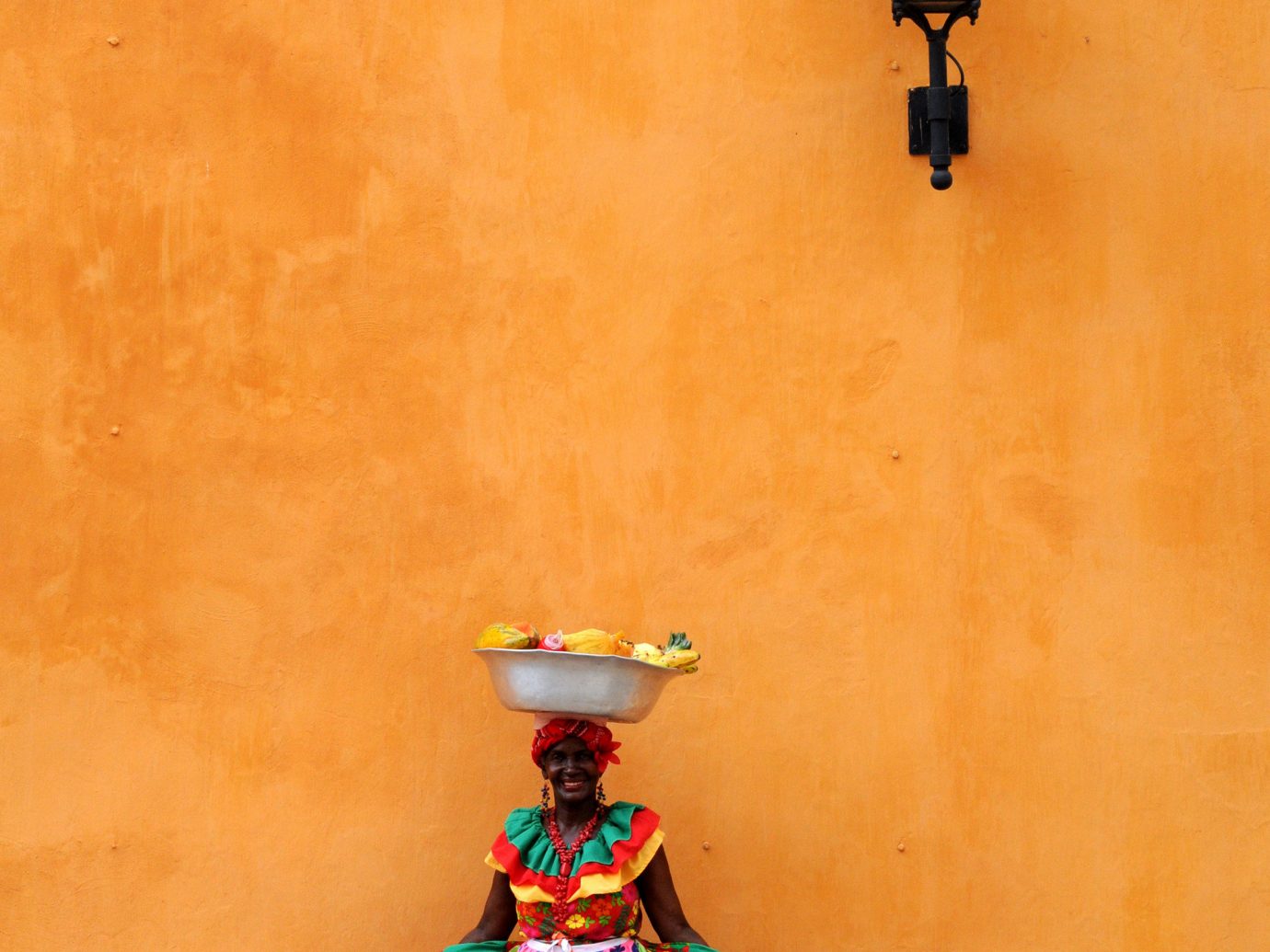 a local in Cartagena standing in front of a yellow wall in a beautiful colorful dress