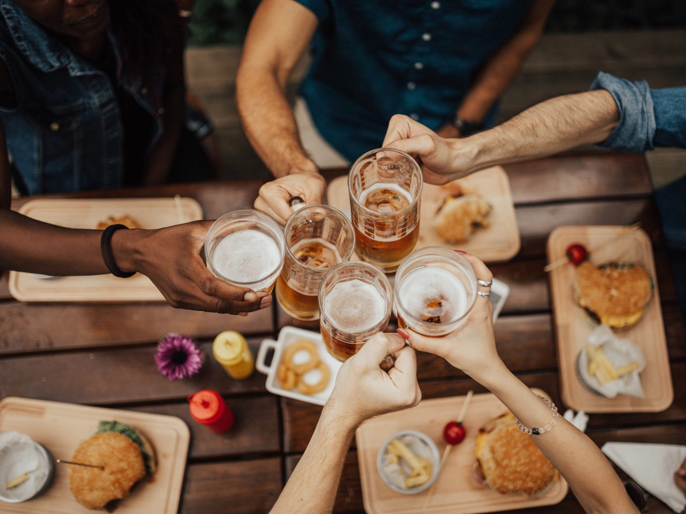 Group of friends toasting their beers with burgers on the table
