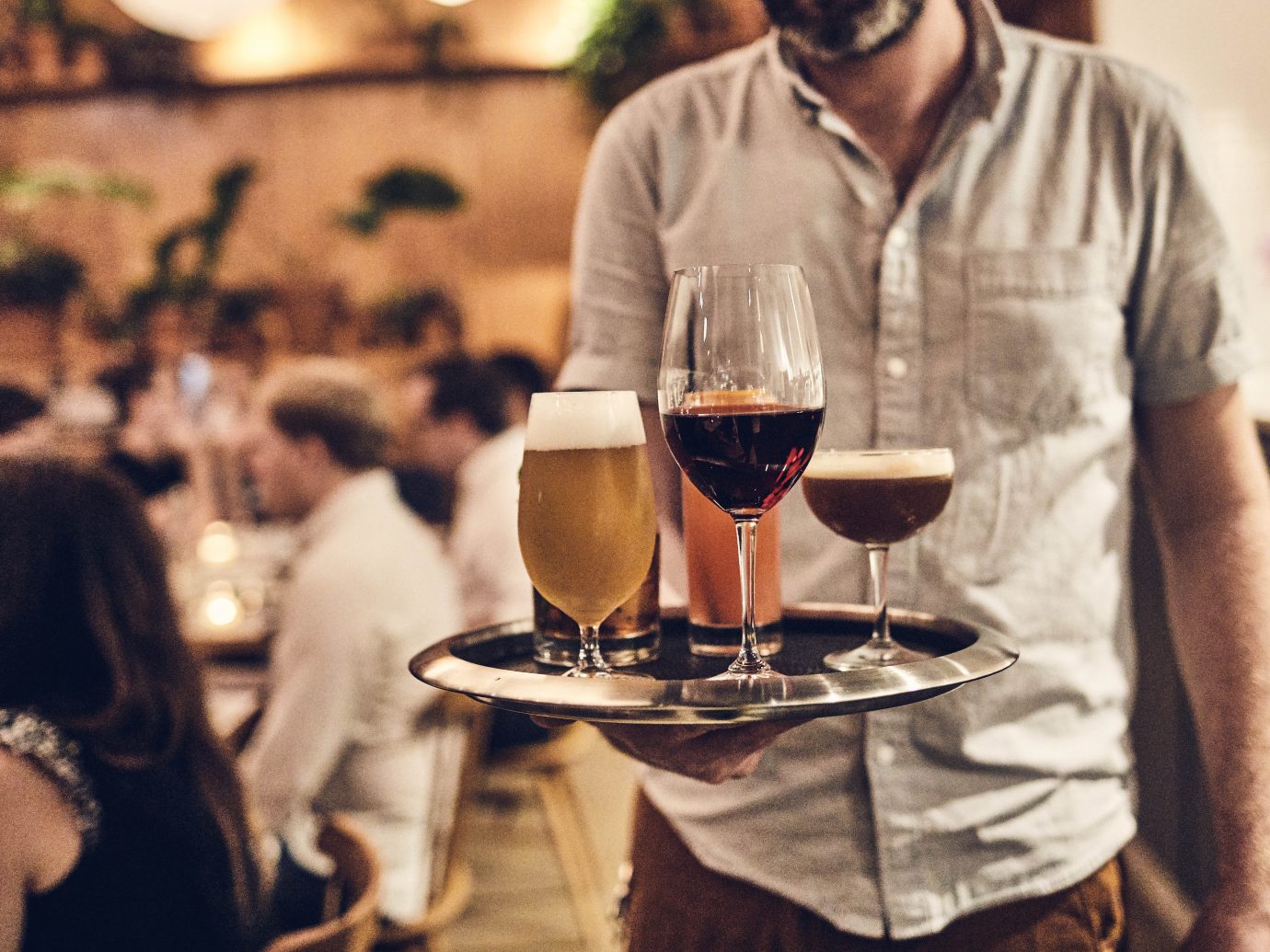 Serving walking to table in packed restaurant interior with tray of drinks