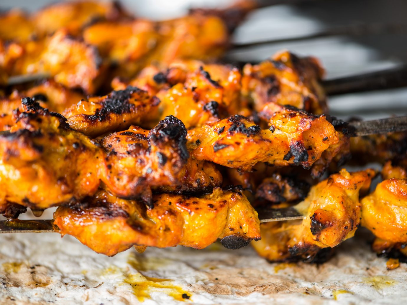 Closeup of freshly grilled chicken tikka masala kebabs on skewers dripping onto a piece of naan flatbread cooked in a Tandoori oven. Dubai, UAE, Middle East, GCC.