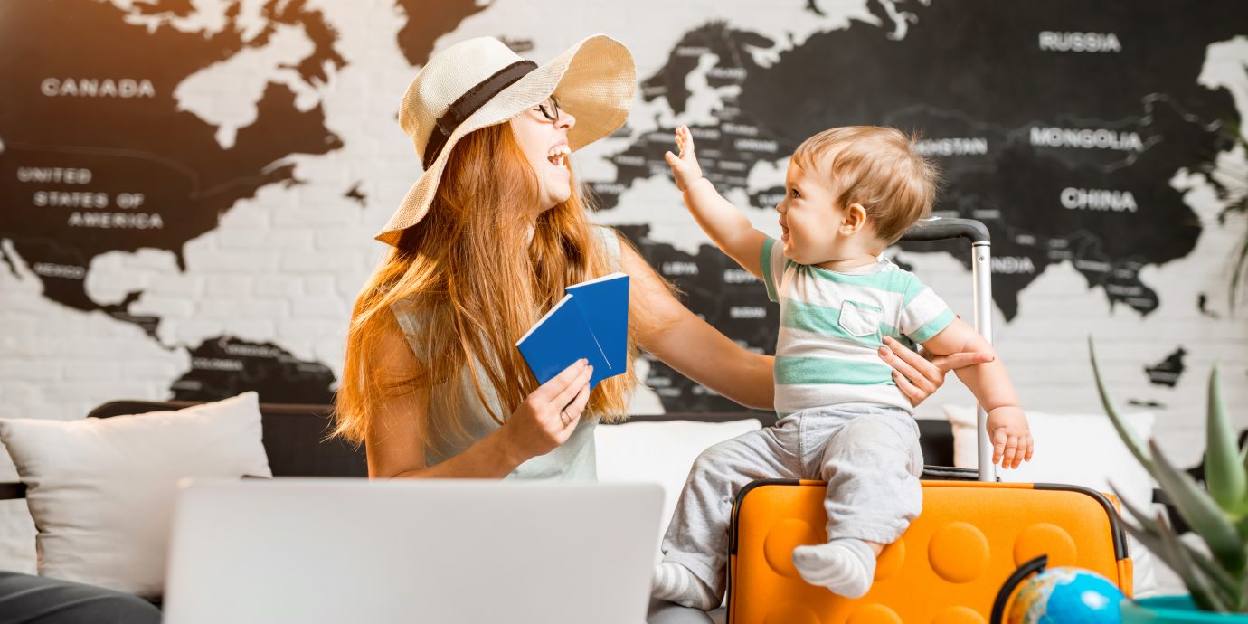 Happy and playful woman with baby boy sitting at the travel agency office with beautiful map on the background ready for a summer vacation