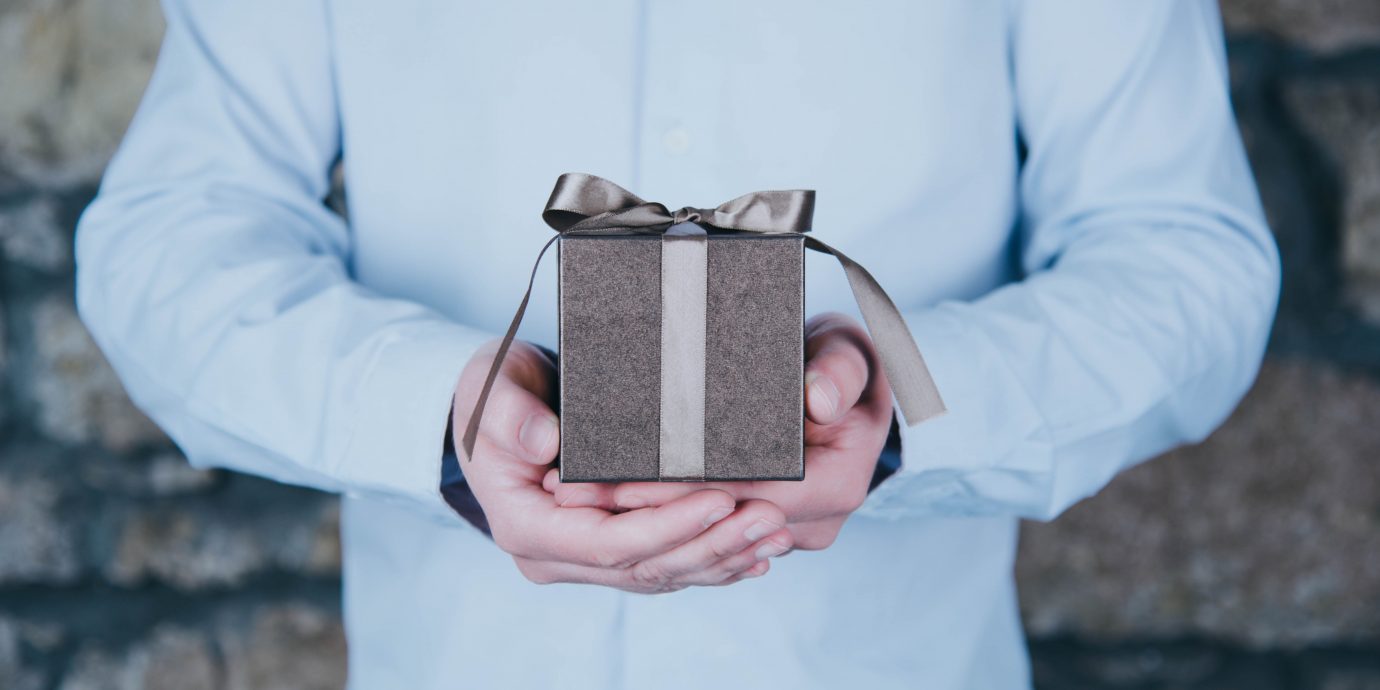 Male hands holding a gift against rustic background.