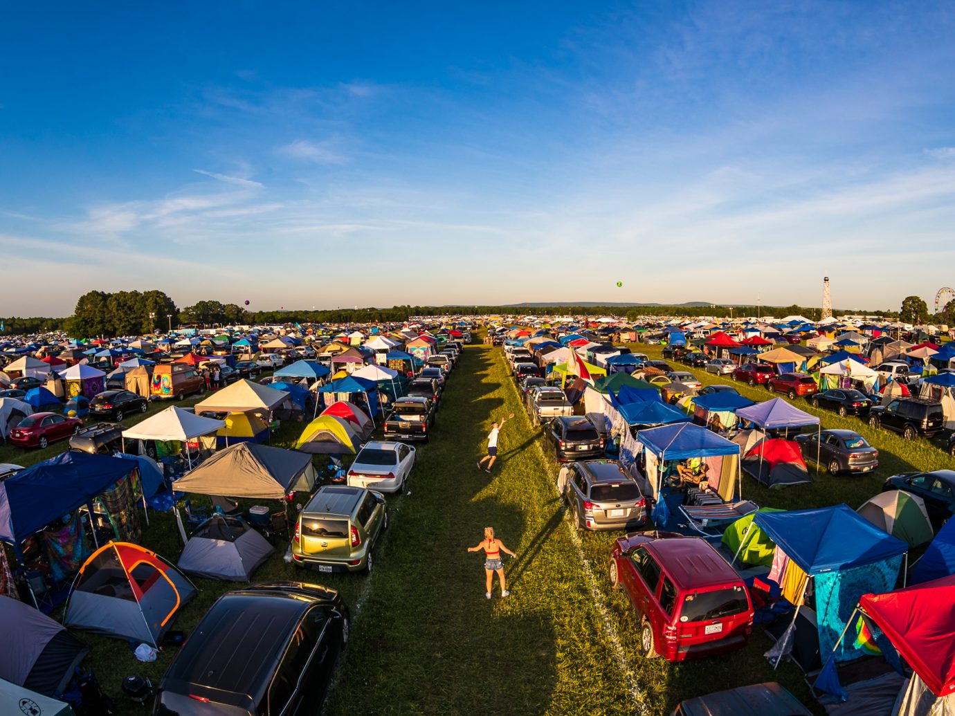 overhead shot of people playing games between a line of cars and tents