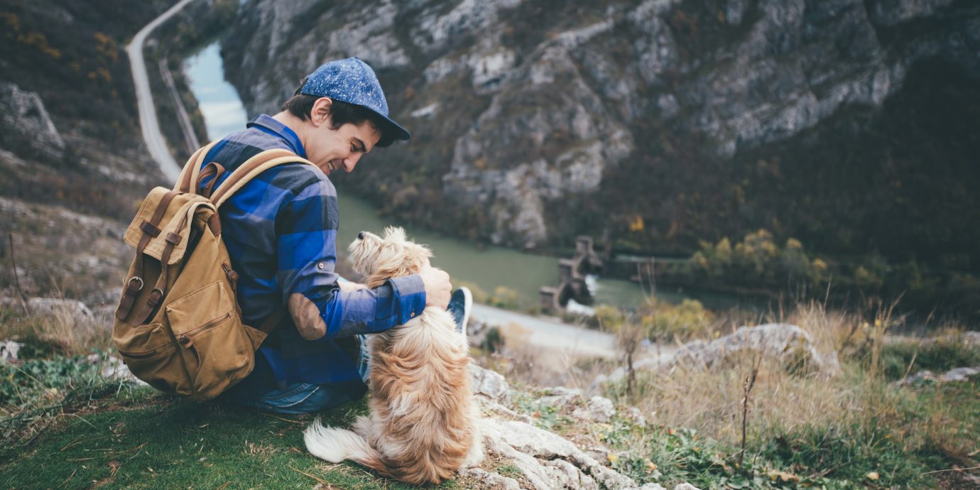 Young traveler with backpack petting dog on a mountain top