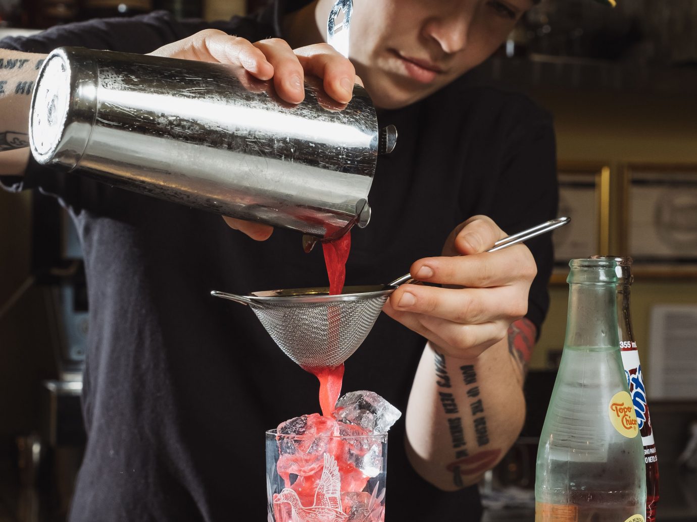 person with tattoos straining a drink