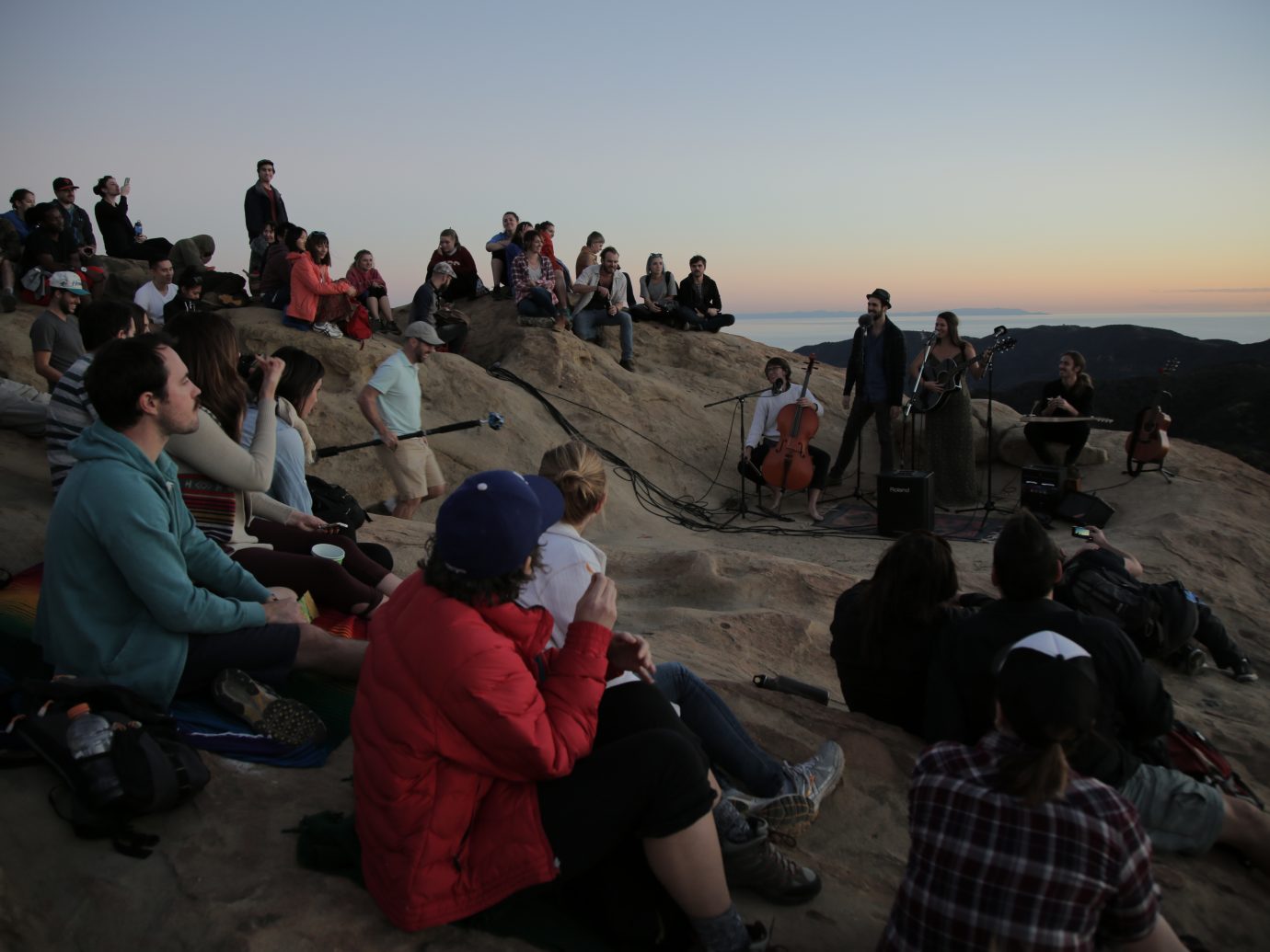crowd at dusk on large rock watching people perform