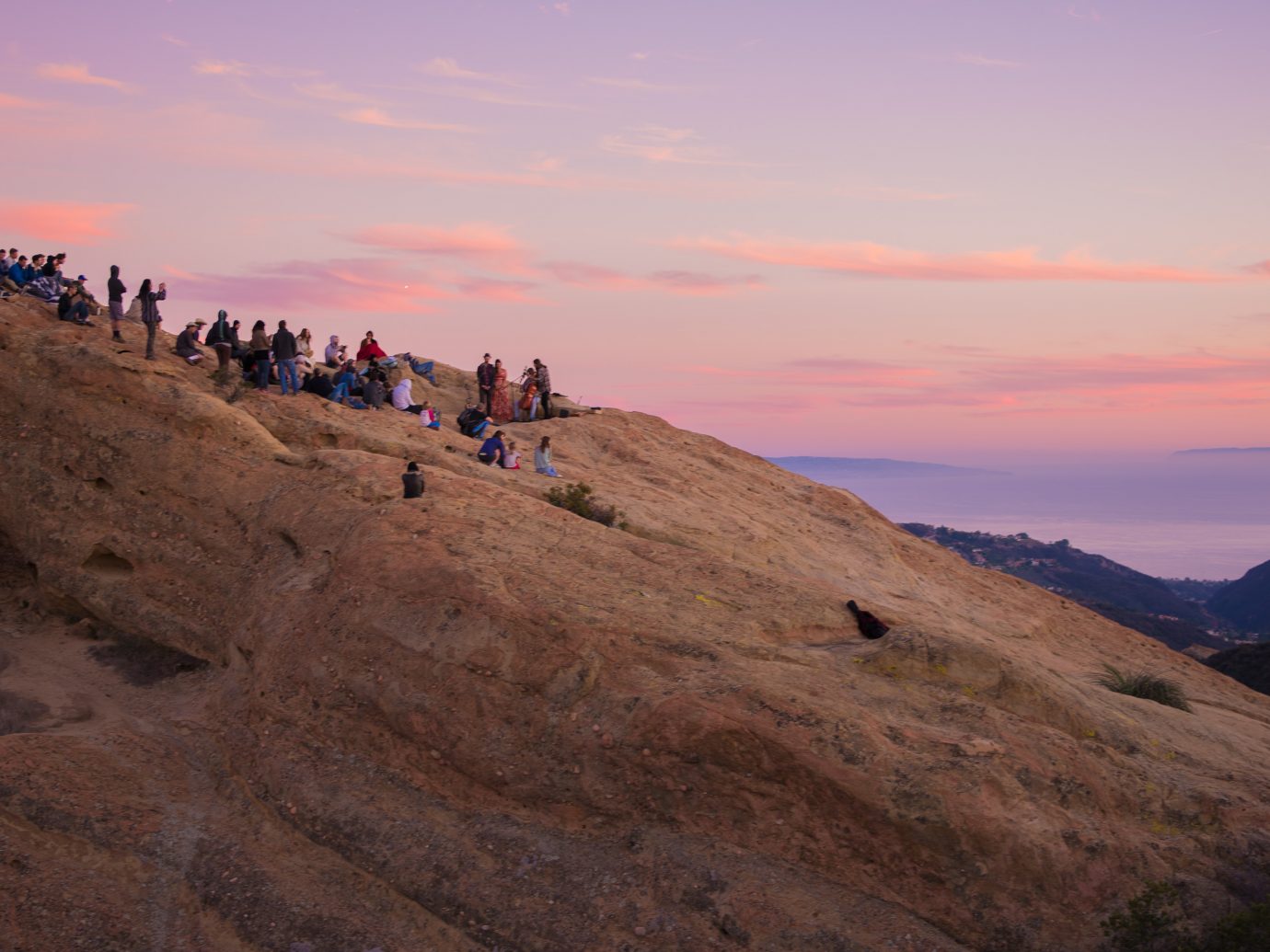 people performing and others watching during sunset on a huge rock