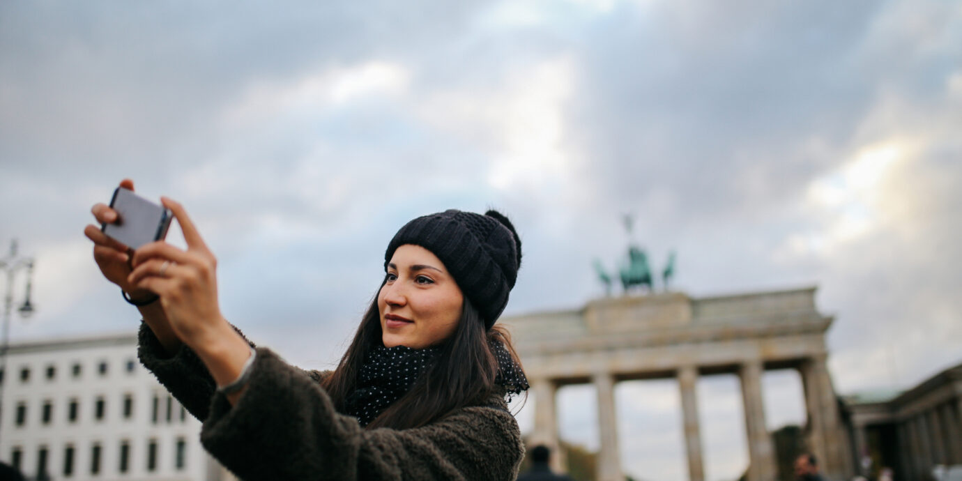 Portrait of a young tourist woman wearing casual clothing, sightseeing, taking selfie images in Berlin Mitte near Brandenburg Gate