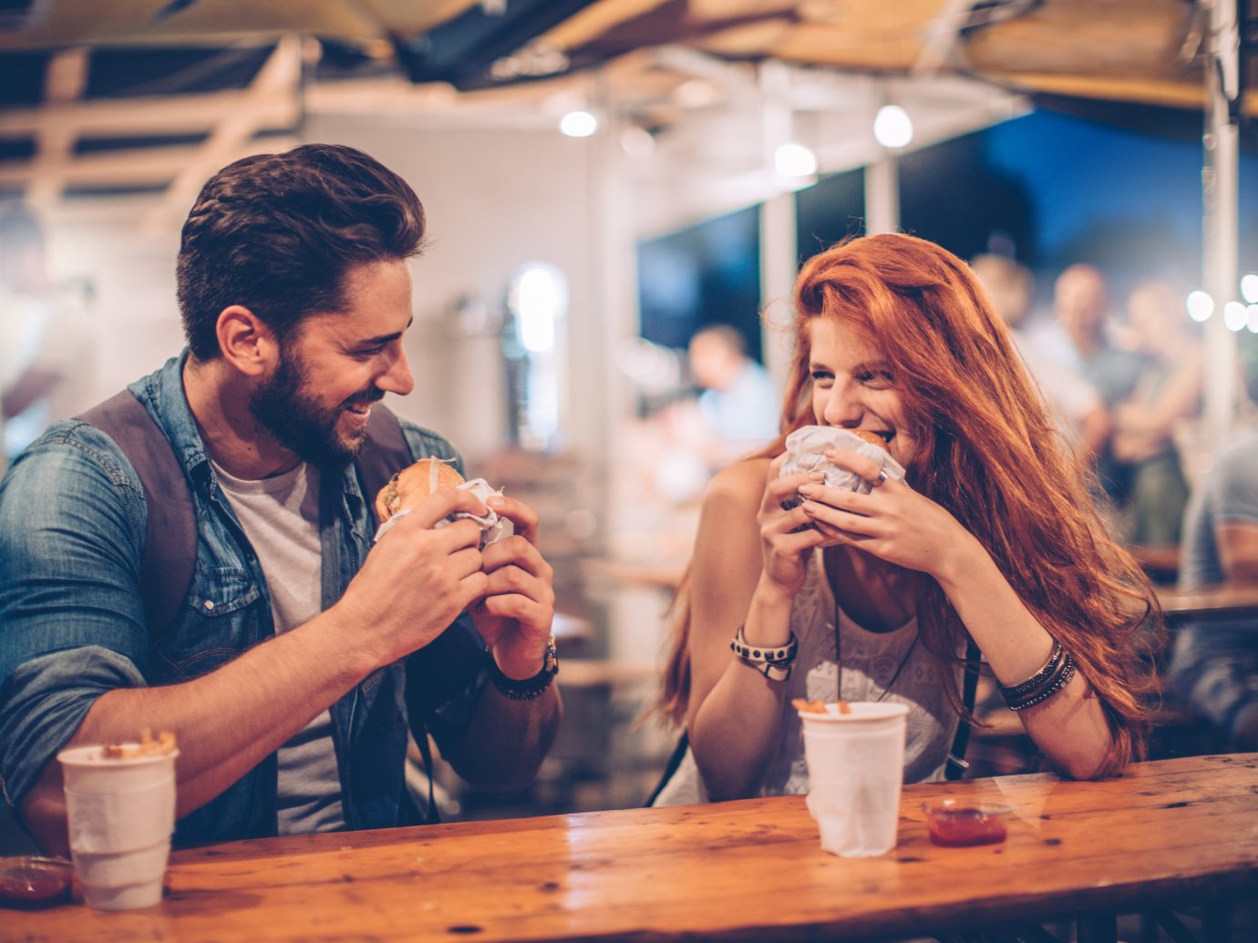 A young couple having snack and drink at an outdoors music festival. Eating burgers with fries and drinking beer.