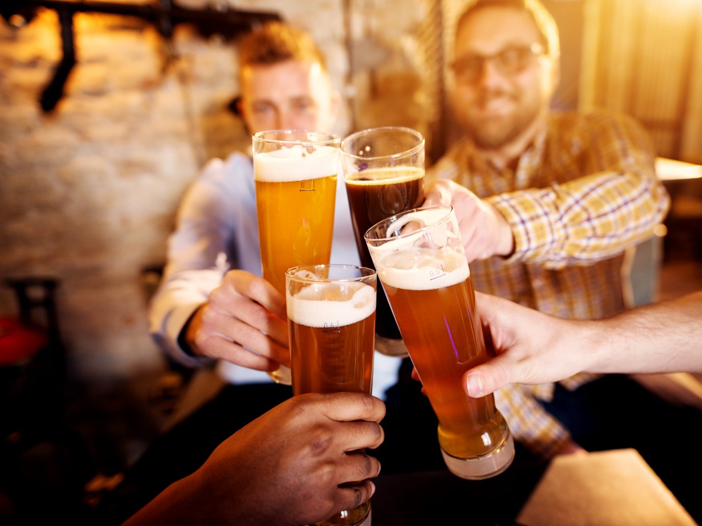 A group of young men clinking glasses with a beer in the sunny pub.