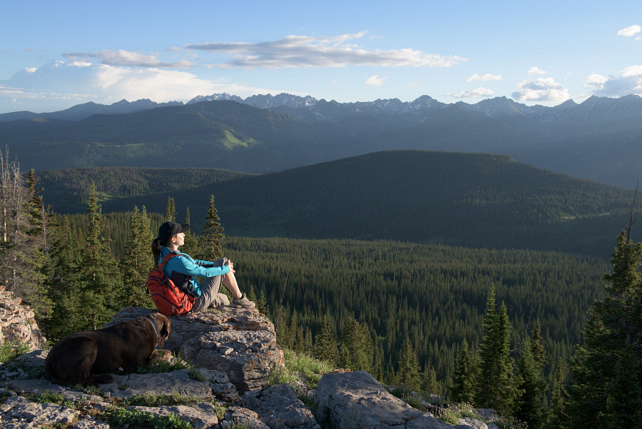 On a clear summer morning, a hiker pauses at the top of Vail Mountain to contemplate the grandeur of a Gore Range sunrise.