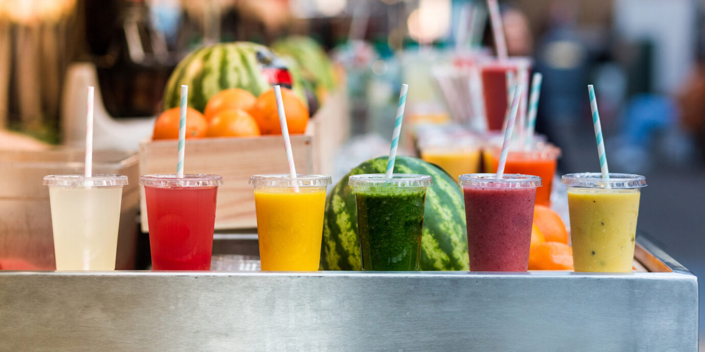 Close up color image depicting freshly made fruit juices and smoothies on display in a row and for sale at a food and drink market in London, UK. Selective focus on the plastic cups containing the fresh smoothies.