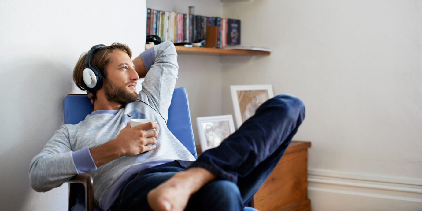 Shot of a young man having coffee while listening to music at home.